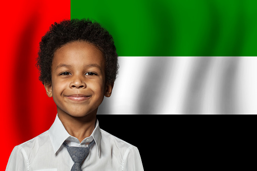 UAE kid boy on flag of United Arab Emirates background. Education and childhood concept