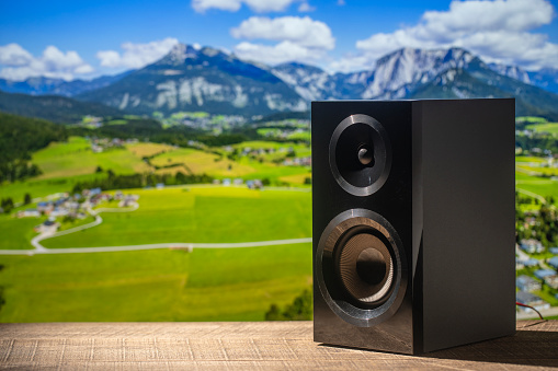 Black acoustic sound speaker on a wooden table against the backdrop of the Alpine mountains in Austria. The musical equipment, close up