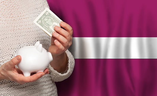 Latvian woman with money bank on the background of Latvia flag. Dotations, pension fund, poverty, wealth, retirement concept