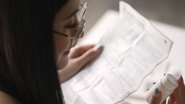 Young Asian woman reading medical instructions before taking medicine.