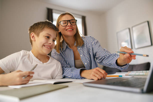 istock Female babysitter is teaching little boy use laptop application during studying 1474308197