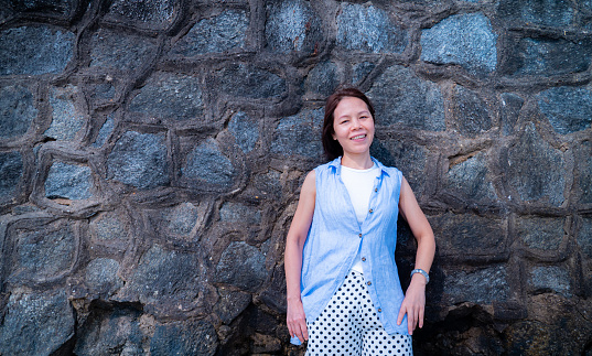 Asian woman leaning against a stone wall and smiling happily. A middle-aged woman with short hair was beautiful, leaning against a stone wall.