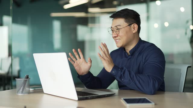 Sonriente hombre de negocios asiático amigable gerente de apoyo trabajador de oficina con gafas mirando la pantalla de la computadora y hablando en línea photo
