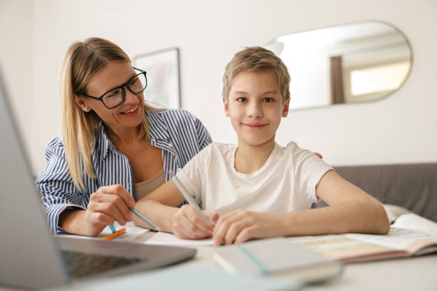 istock Smiling mom helping her son doing homework studying online using laptop in home 1474310943