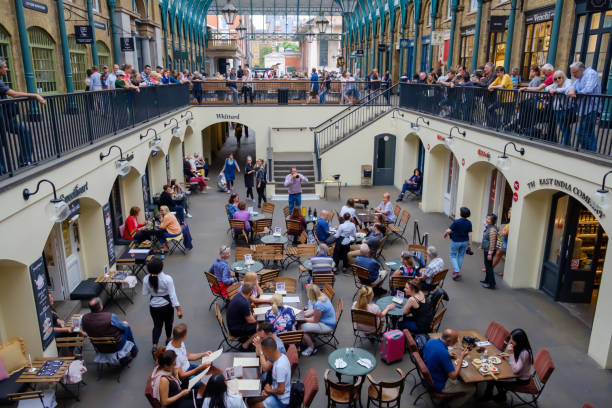 People dining outdoors at Covent Garden Market, London. Lively scene with restaurants, sunshine, and social atmosphere in historic market square.