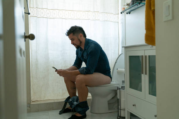 istock Young man watching videos on his smart phone while being at the bathroom 1474314943