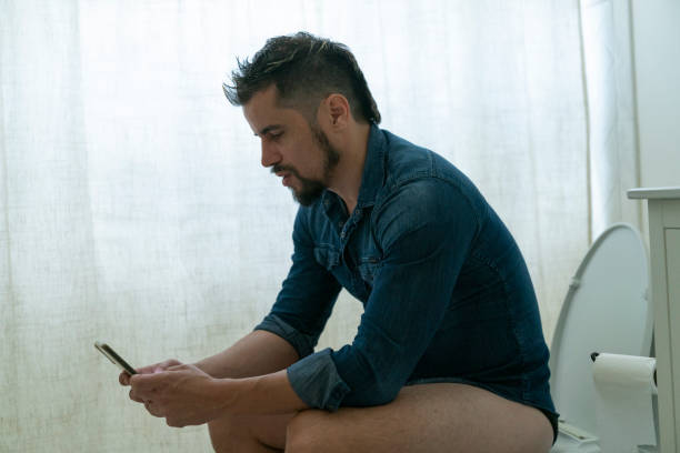 istock Young man watching videos on his smart phone while being at the bathroom 1474314944