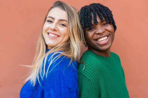 A caucasian blonde girl and an African-American boy standing shoulder to shoulder, wearing vibrant-colored sweaters. Friendship and inclusivity concept
