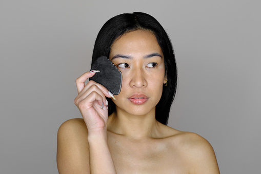 medium shot of a confident Filipino woman doing a face treatment in a grey background studio shot