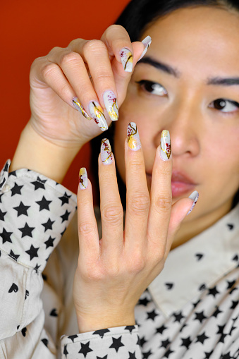 front view shot of a confident Filipino woman showing her decorated nails in an orange background studio shot