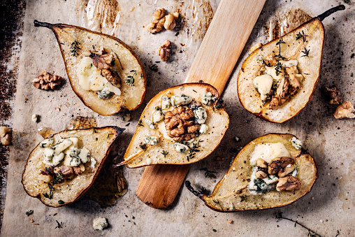 Baked pears with walnuts and gorgonzola cheese. The pears have been sliced in halves, seasoned with salt pepper and thyme and brushed with a small amount of olive oil. They have been baked at 375/180 degrees for around 15 minutes, removed from the oven the cheese and walnuts are added before being placed back in the oven for another 10 minutes or so. Colour, horizontal format with some copy space.