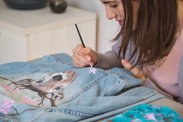 Caucasian woman painting a design of a deer and flowers in a denim jacket. stock photo
