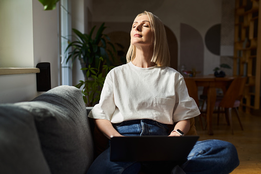 Mindfulness concept. Worek life balance. Adult woman with laptop relaxing on the sofa with closed eyes