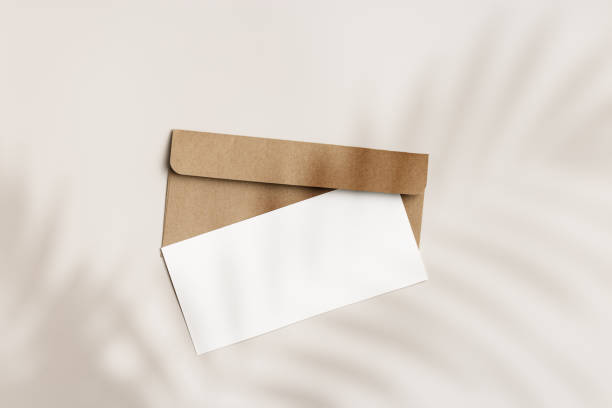 istock Blank paper card mock up and craft envelope on beige background and palm leaf shadow. White empty invitation on table. Minimal fashion lifestyle photo. Summer Flat lay, top view, copy space. 1474326303
