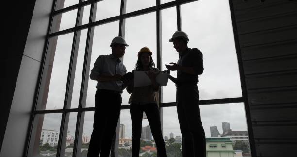 istock Silhouette of Asian group Architect and engineer construction workers on plans with a blueprint while working for teamwork. Architects discussing business plans 1474327462