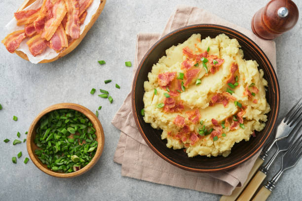 istock Mashed boiled potatoes. Bacon mashed potatoes with green onion, pepper and cheddar cheese in bowl on light old wooden backgrounds. Delicious creamy mashed potatoes. Top view. 1474327509