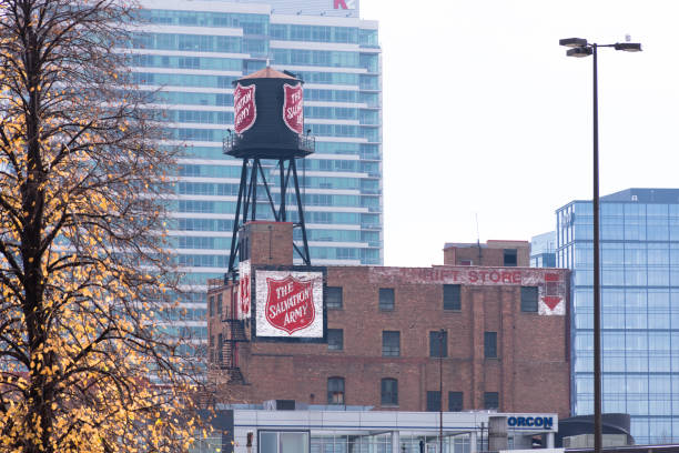 Red and white Salvation Army sign painted on side of four-story brick building and also water tower, Chicago, with autumn tree and high rise building in background. stock photo