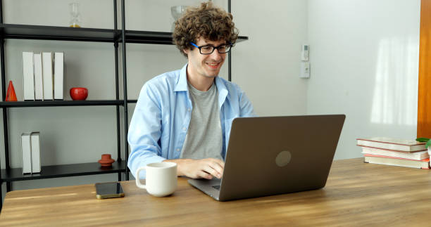 istock Smiling man with eyeglasses using laptop working at home 1474338508