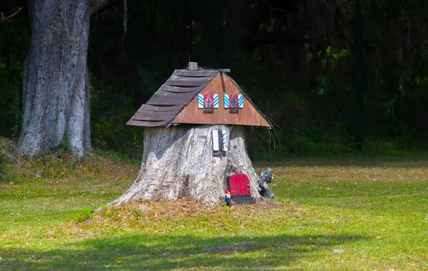 old tree stump turned into a garden fairy gnome house in the middle of Grass field with tiny bigfoot