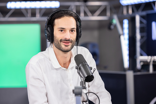 portrait of a radio or tv host sitting in a studio in front of his microphone. it's a live broadcast and he wears headphones over his ears