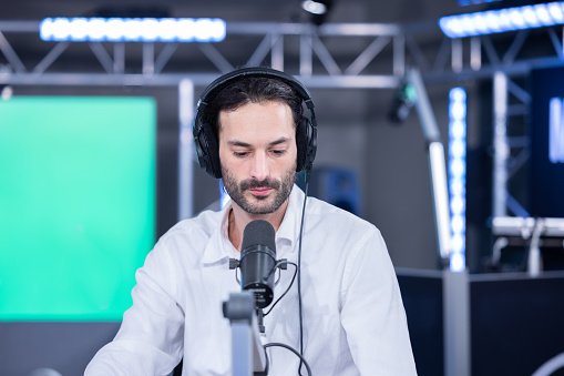 portrait of a radio or tv host sitting in a studio in front of his microphone. it's a live broadcast and he wears headphones over his ears