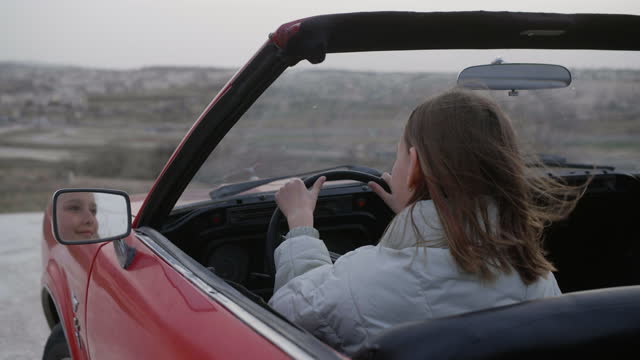Young girl in convertible red car looking at mirror sending air kiss herself.