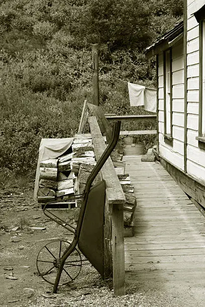 A photograph of a wheelbarrow in an old fashioned setting (Barkerville, British Columbia, Canada).  This photograph was converted to black and white with sepia toning added to give it an old fashioned feel.