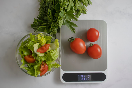 Plate with salad, kitchen scales on a light background