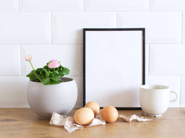 istock Spring still life. Blank picture frame mockup on wooden table background. Easter composition with Leucanthemum vulgare, Bellis perennis flowers in a pot, hen eggs, and silk ribbon. Farmhouse, Scandinavian interior. 1474349998