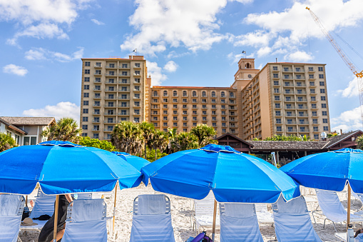 Naples, USA - December 28, 2021: Vanderbilt beach in Florida southwest with Ritz-Carlton hotel resort building exterior and beach chairs with umbrellas view