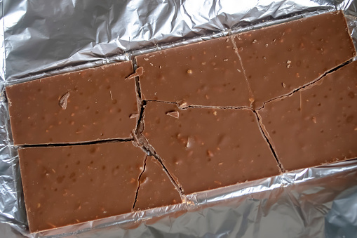 On the aluminum foil is a chocolate bar. Chocolate on foil. pieces of broken chocolate. Milk chocolate is a broken bar.