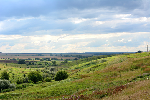 A grassy rolling hill with a cloudy and rainy sky in the background