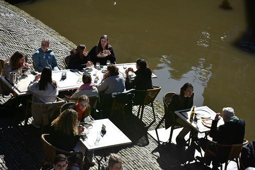 Utrecht City Canal In The Netherlands Europe, People Sitting Down, Talking To One Another, Eating And Drinking In A Restaurant Scene During Winter Season