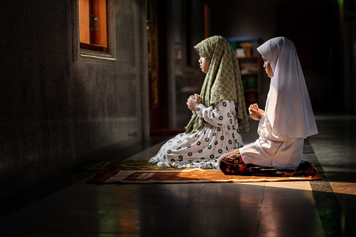 Muslim girl in hijab sitting in the mosque praying