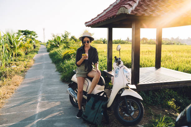 Millennial female user checking location information during online GPS tracking via modern cellphone gadget, travel girl resting on rent moped connecting to roaming internet for browsing website usuario femenino millennial que verifica la información de ubicación durante el rastreo gps en línea a través de un moderno dispositivo de teléfono celular, chica de viaje descansando en un ciclomotor de alquiler que se conecta a internet en roaming p