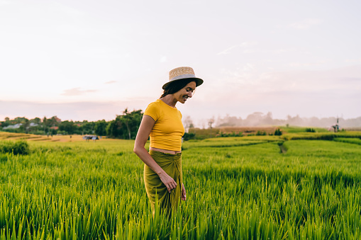 Side view of unrecognizable woman in trendy wear smiling while spending time in bright green garden during vacation on Bali