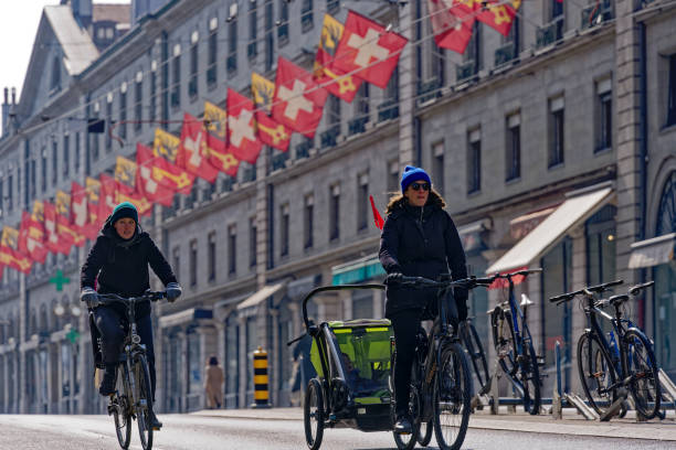 Women raiding bicycles at Swiss town with trailer. Two female cyclists with child trailer at Swiss City of Geneva on a sunny late winter day. Photo taken March 5th, 2023, Geneva, Switzerland. geneva switzerland stock pictures, royalty-free photos & images