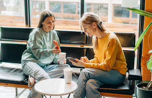 Two cheerful laughing women friends in a coffee shop communicate and chat on the phone.