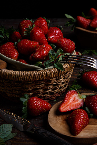 Mature red strawberries on a black table and fresh ripe strawberries in a wooden basket