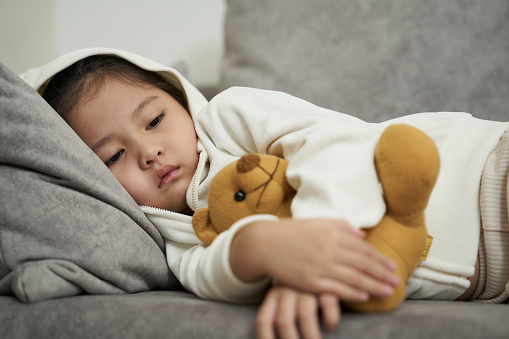 Sick Toddler girl with high flu and cold fever lying down on sofa