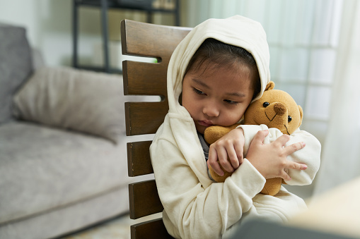 Unwell  Asian Toddler girl hug teddy bear with high fever and cold at home.