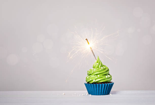 istock Green cupcake with sprinkles and lit sparkler on a white grey background. 1474361927