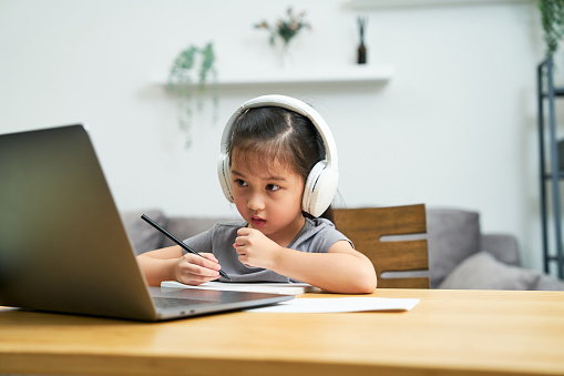 Asian home school girl wearing wireless headphone listening and learning  E-learning class on laptop computer at home but got a fever and cold. Unwell Children.