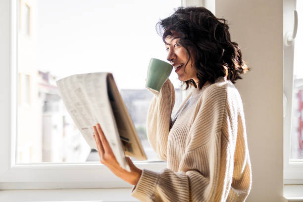 Young woman drinking cup of coffee reading newspaper Beautiful young woman drinking cup of coffee reading newspaper reading newspaper stock pictures, royalty-free photos & images