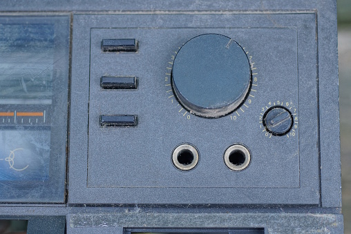 one black round plastic large volume control with small buttons on the gray panel of an old tape recorder