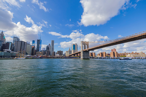 Brooklyn bridge from East river at sunset with flare. Wall street area, Freedom tower and the Beekman tower are seen behind it.