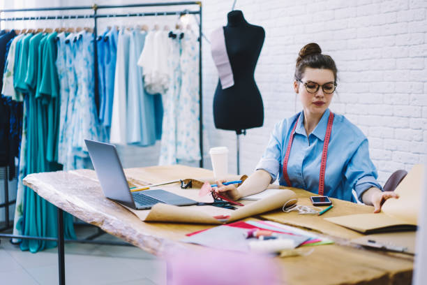 istock Focused young dressmaker working with new order sitting at table in workshop 1474377759