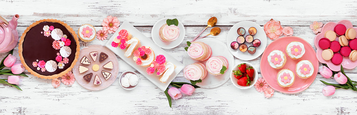Mothers Day table scene with a variety of desserts and sweets. Top down view on a white wood banner background. Pink flowers theme.