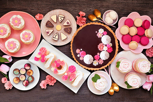 Mothers Day table scene with assorted desserts and sweets. Overhead view on a dark wood background. Pink flowers theme.