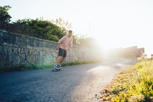 Skilled teen male skater in casual street style wear riding on board on road enjoying active hobby free time, handsome caucasian hipster guy enjoying practice on longboard resting on weekends